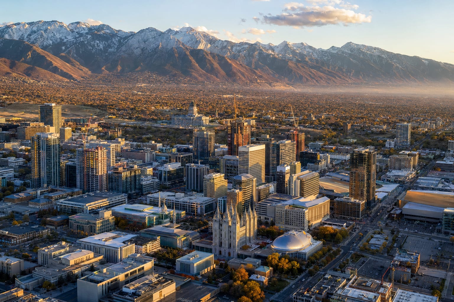 Aerial view of downtown Salt Lake City at golden hour with the Utah State Capitol, Salt Lake Temple, and the snow-capped Wasatch Front.